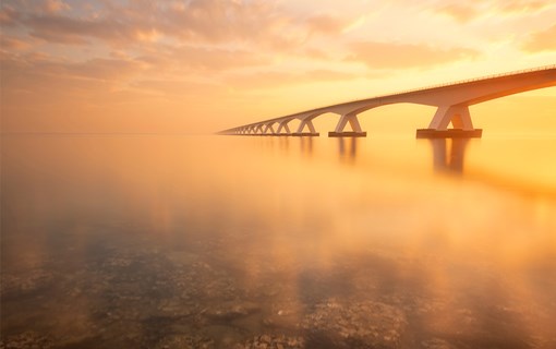 Zeelandbrug tijdens zonsondergang met op de voorgrond de zee